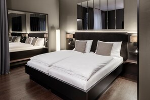 A modern hotel room with a large bed, bedside lamps, and a mirror. - Hotel AMANO Düsseldorf (Düsseldorf)