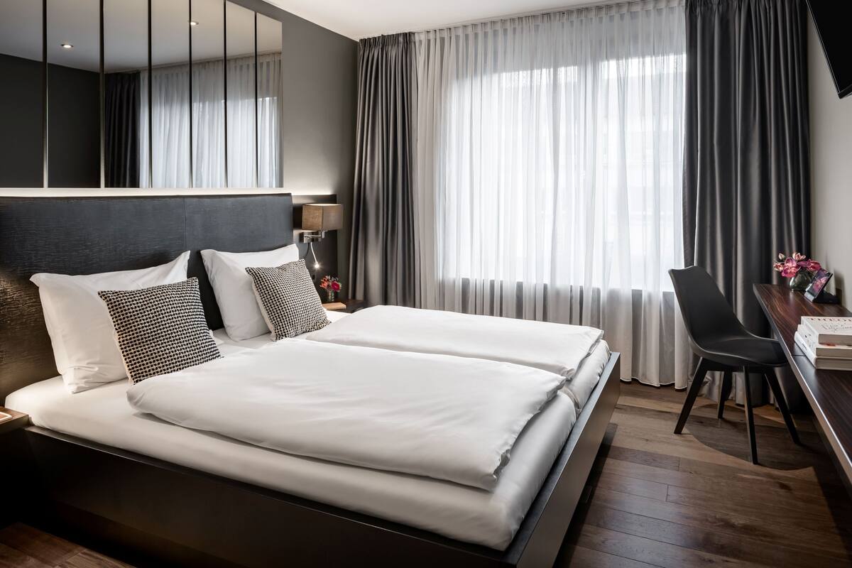 A modern hotel room with a large bed, a desk, and a chair.