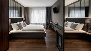 Quarto de hotel moderno com uma cama grande, uma mesa de trabalho, uma cadeira e uma TV fixada na parede.