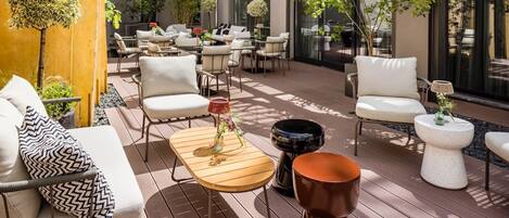 Un patio al aire libre con varios conjuntos de asientos, incluyendo sofás y sillas, y diversos elementos decorativos como plantas y mesas.