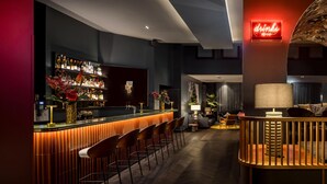 Uma área de bar moderna com um balcão extenso, banquetas e uma prateleira repleta de bebidas.