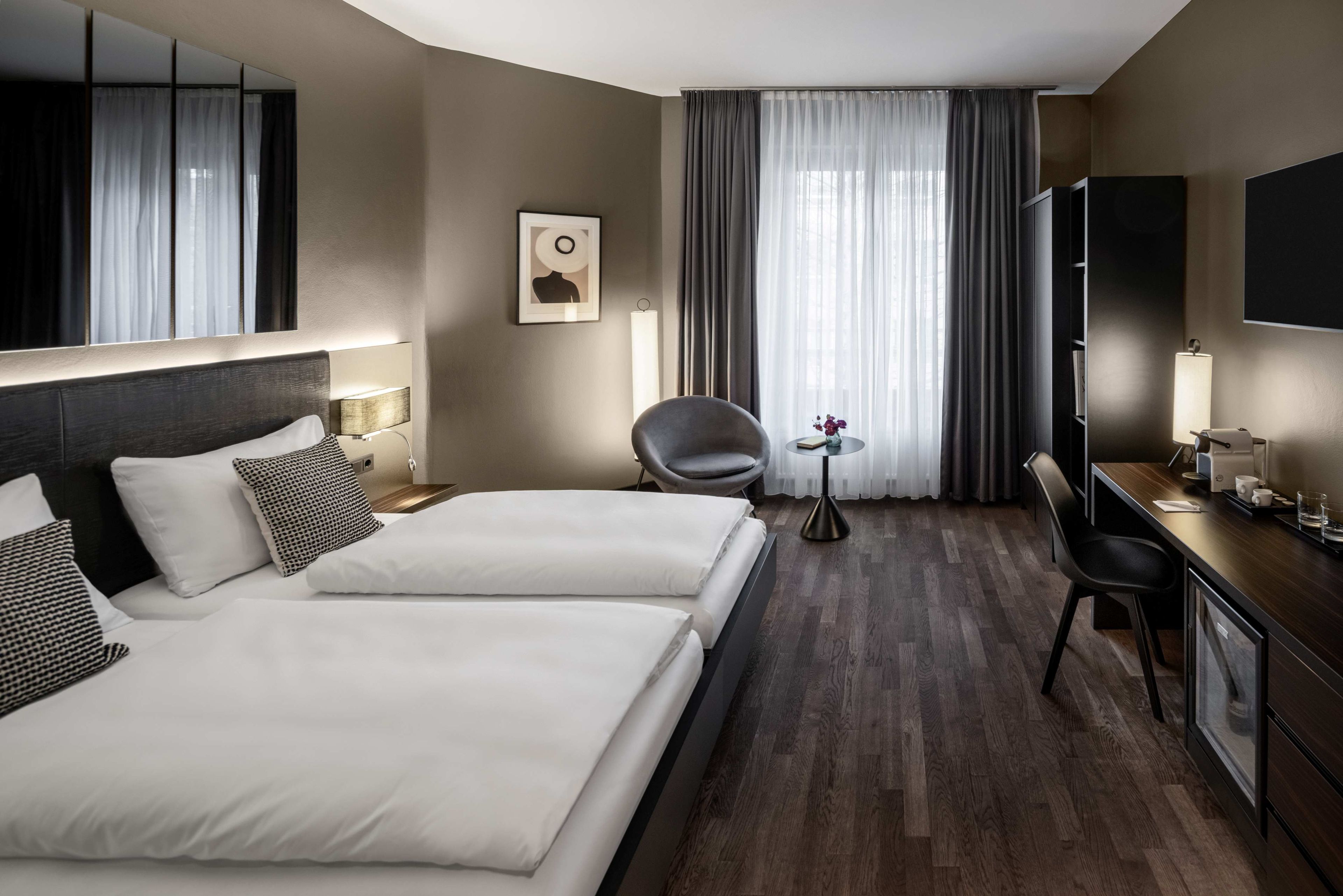 Habitación de hotel con dos camas, un escritorio, una silla, un televisor y un ventanal con cortinas.