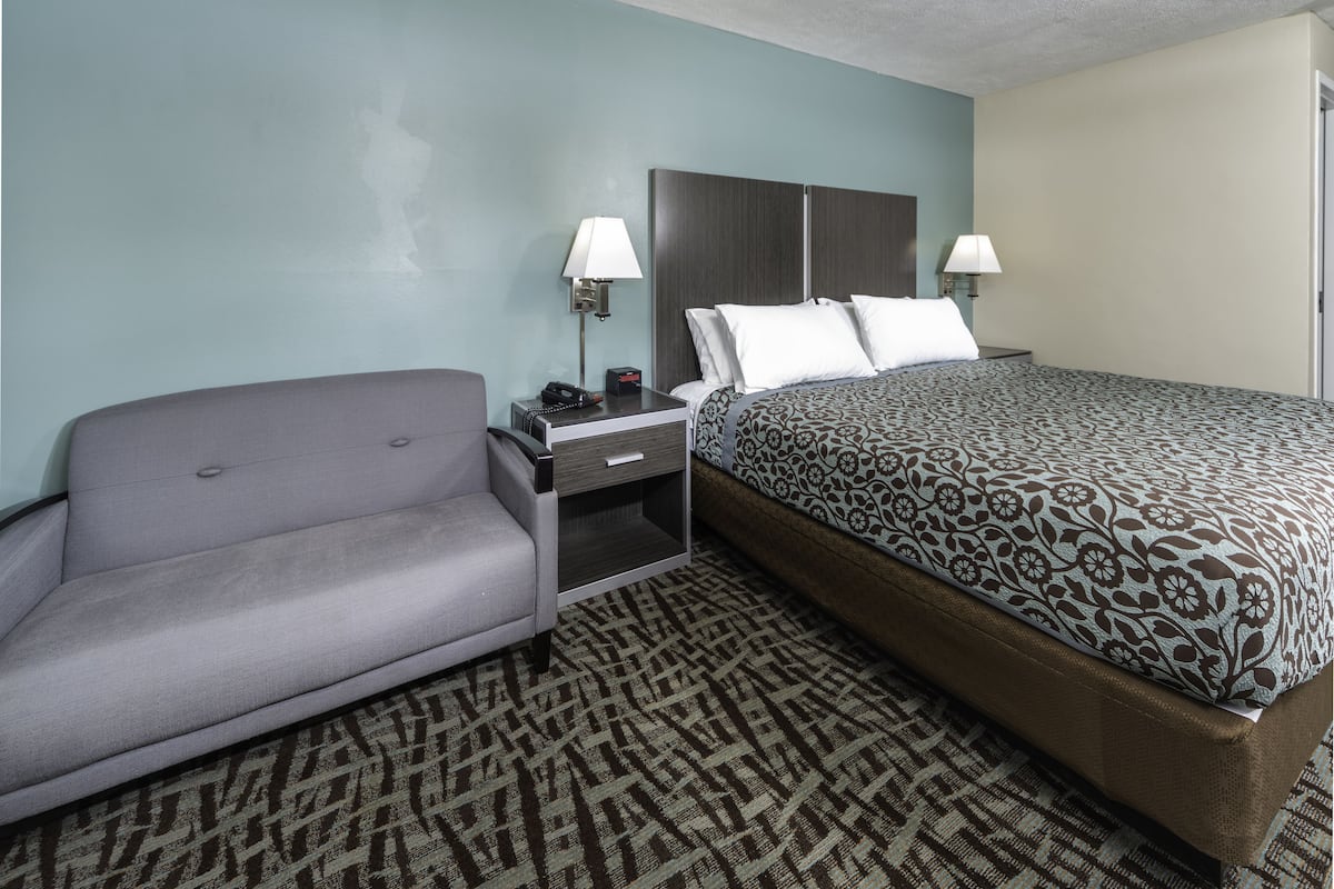 A hotel room with a bed, a sofa, a nightstand, and a lamp.