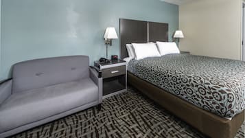 Quarto de hotel com cama, sofá, mesa de cabeceira e luminária.