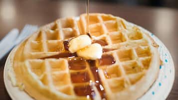 Une vue rapprochée d’une gaufre nappée de sirop, avec une quenelle de beurre posée sur une assiette.