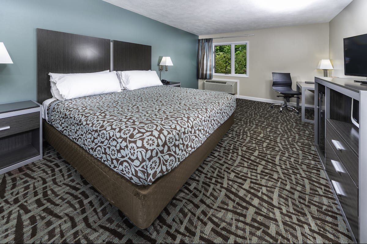 A hotel room with a large bed, a desk with a chair, a television, and a window with curtains.