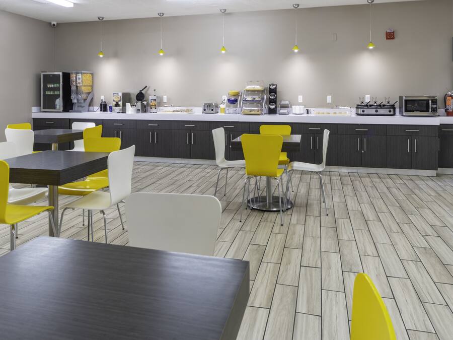 A modern kitchen with a white countertop, stainless steel appliances, and yellow chairs.