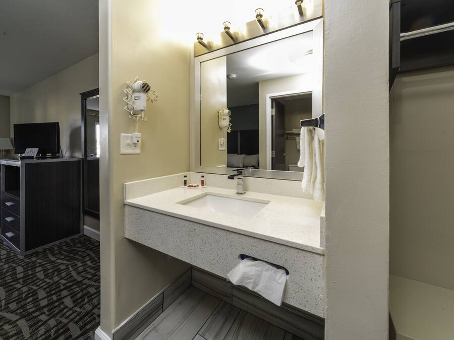 A hotel bathroom with a large mirror, a sink, a towel rack, and a hairdryer on the wall.