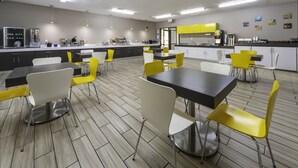 Un moderno comedor con mesas y sillas, una cocina al fondo y un piso de baldosas limpias.