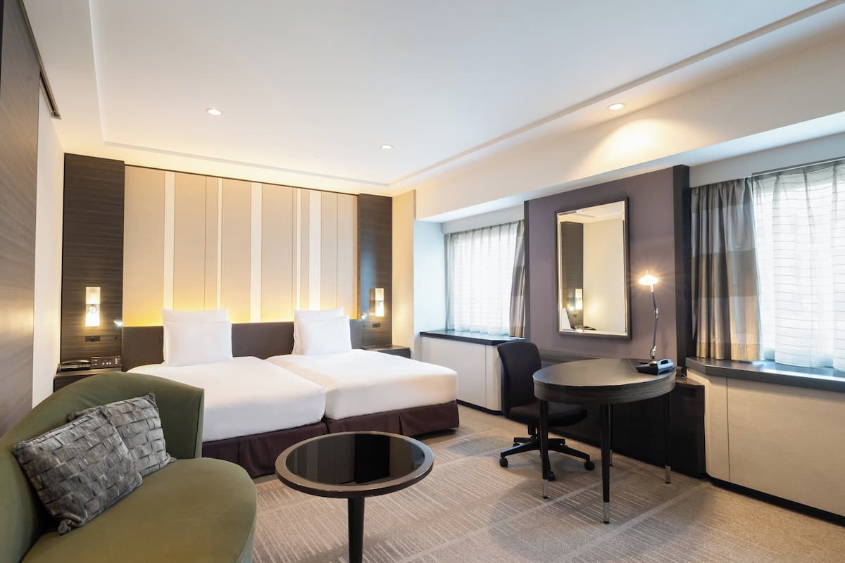 Une chambre d’hôtel avec un lit double, un canapé vert, une petite table ronde, un bureau et un grand miroir.