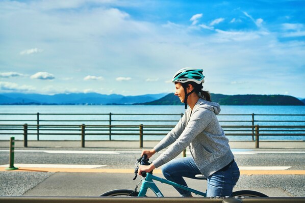 A person riding a bicycle on a paved path by a body of water with mountains in the background.