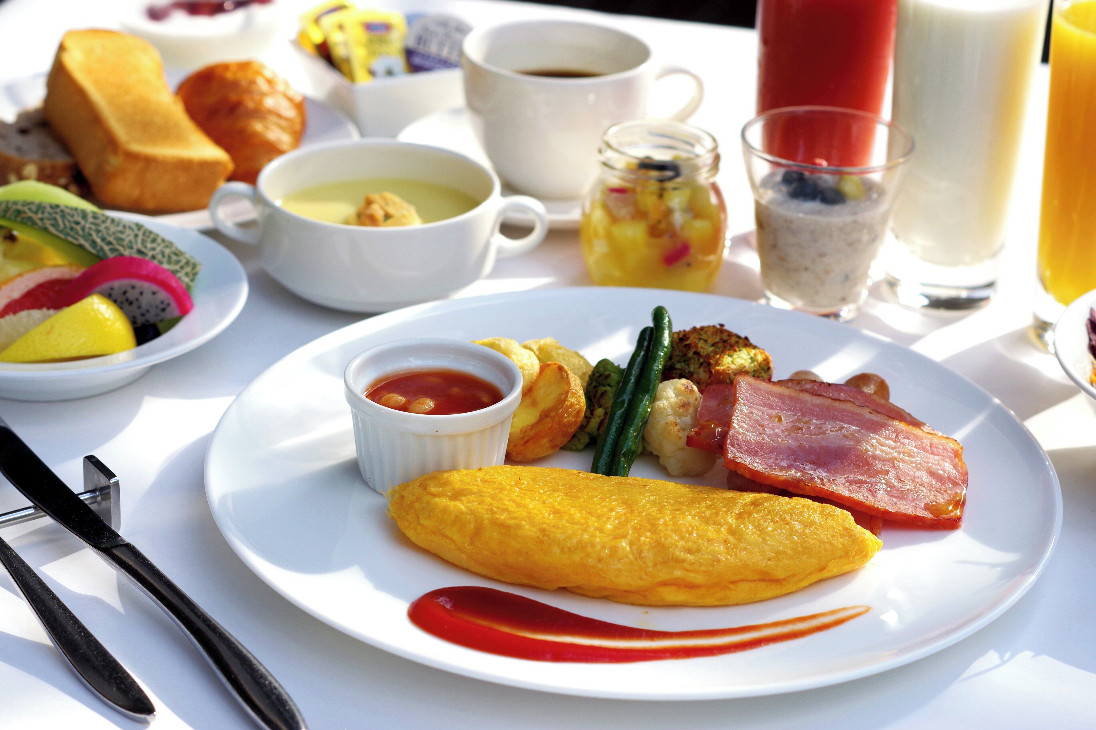 A breakfast plate with eggs, ham, and vegetables, accompanied by a cup of coffee and a glass of orange juice.