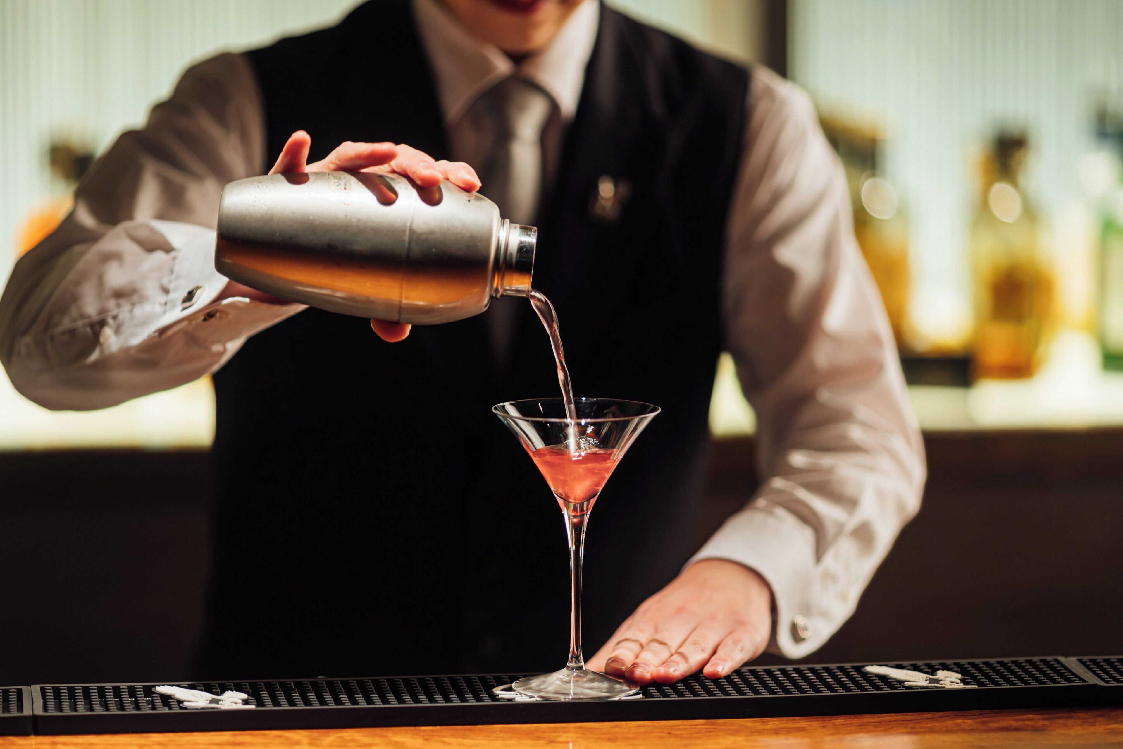 Ein Barkeeper gießt ein Getränk in ein Martini-Glas.