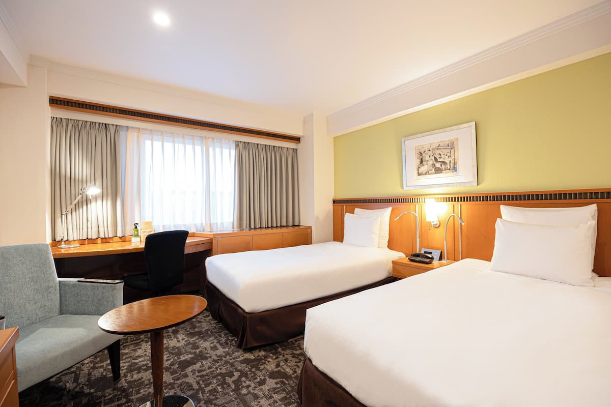 Une chambre d’hôtel avec deux lits, un bureau, une chaise et une petite table.