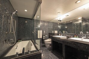 A modern bathroom with a glass-enclosed shower, a bathtub, two sinks, and a toilet.