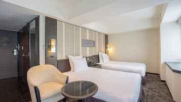 Una habitación de hotel con dos camas, una mesita redonda pequeña, un sofá y un televisor fijado a la pared.