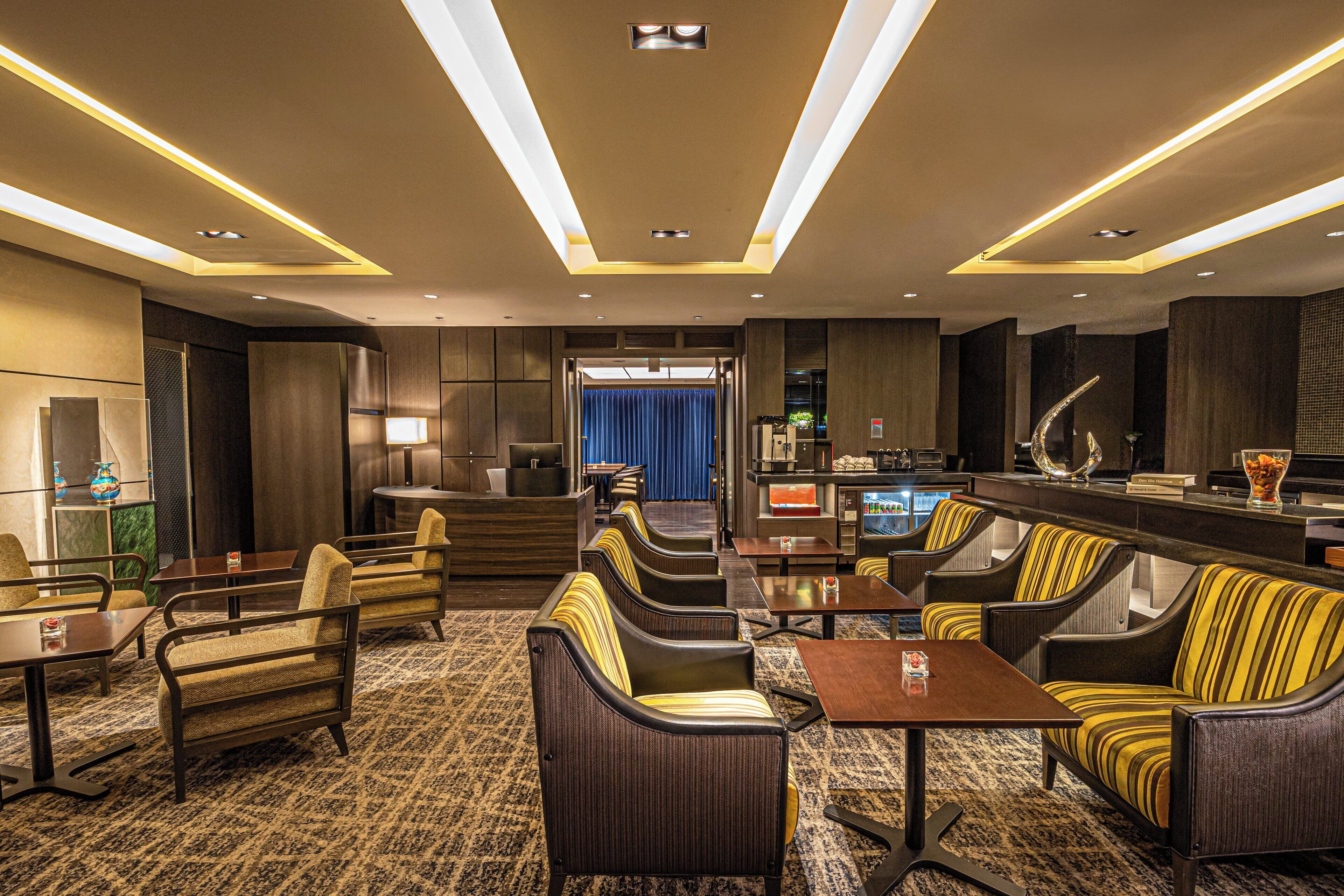 A modern hotel lobby with seating areas, a bar, and a view into the dining area.