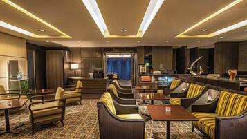 A modern hotel lobby with seating areas, a bar, and a view into the dining area.