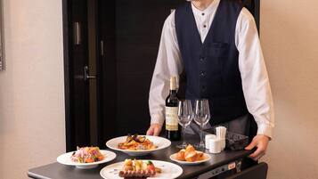 A hotel room with a dining table set with plates of food, a bottle of wine, and glasses.