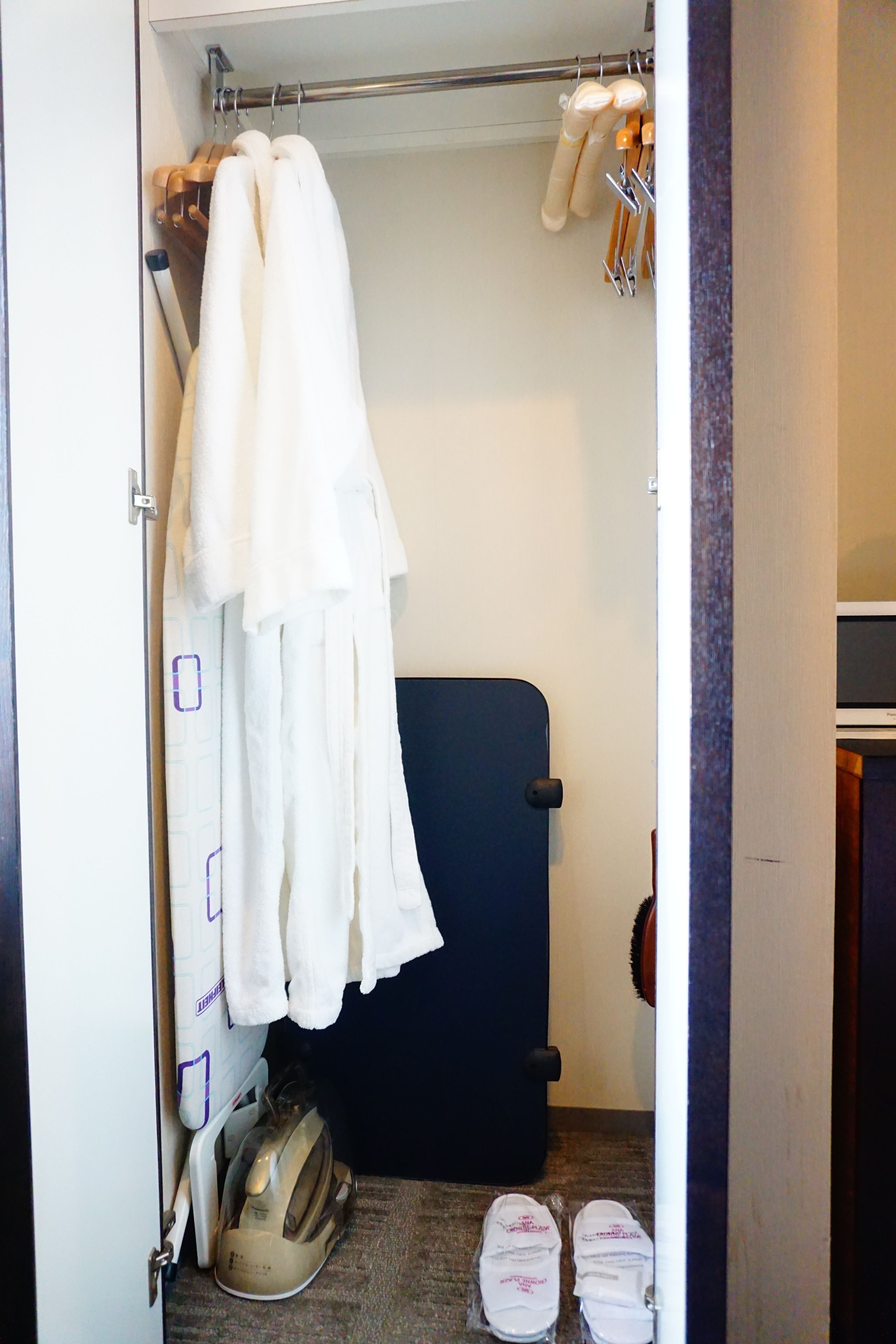 Ein kleiner begehbarer Kleiderschrank mit einem schwarzen Koffer, einem Dampfbügeleisen und einem Paar Schuhe.