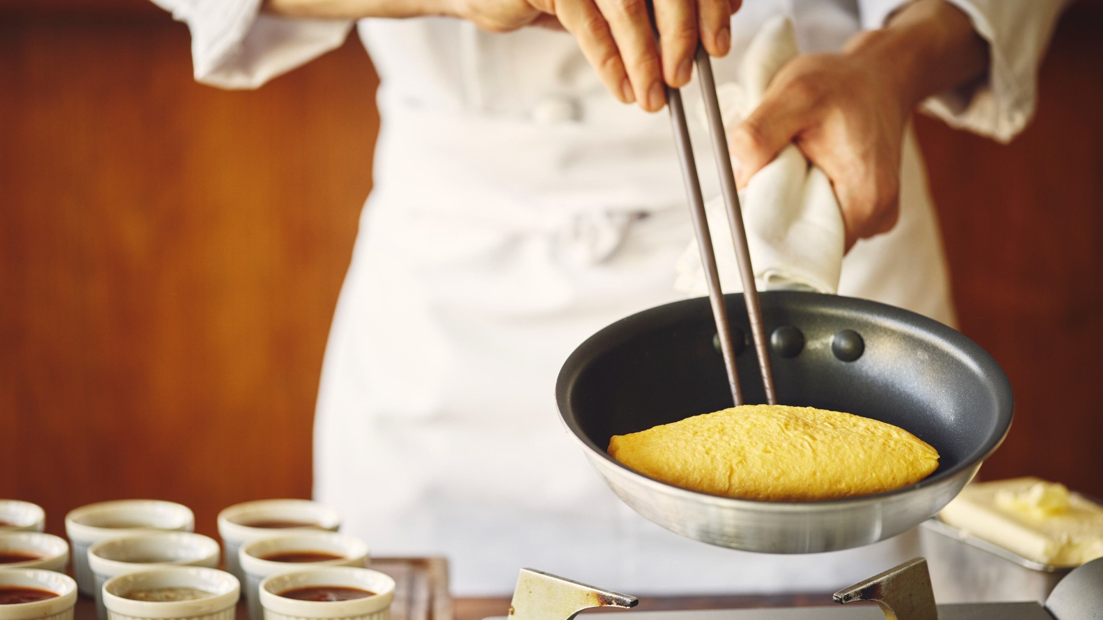 A person cooking in a kitchen with a frying pan on a stove.