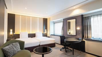 Quarto de hotel com cama de casal, sofá verde, pequena mesa redonda, escrivaninha e um espelho grande.