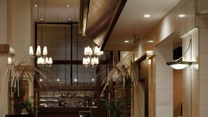 Um saguão de hotel com carpete vermelho, área de estar e um bar ao fundo.