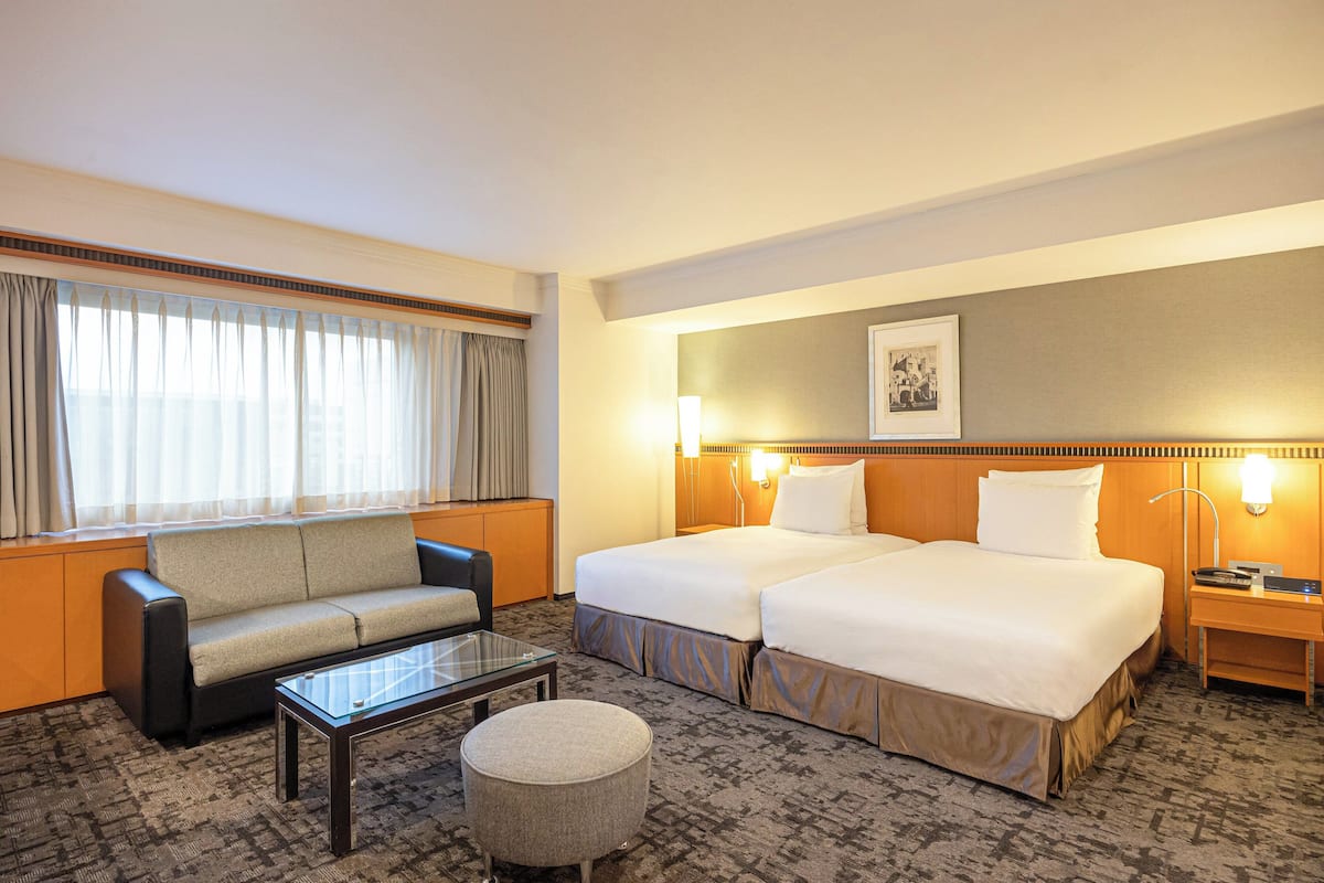 Une chambre d’hôtel avec deux lits, un canapé, une table basse et une lampe.