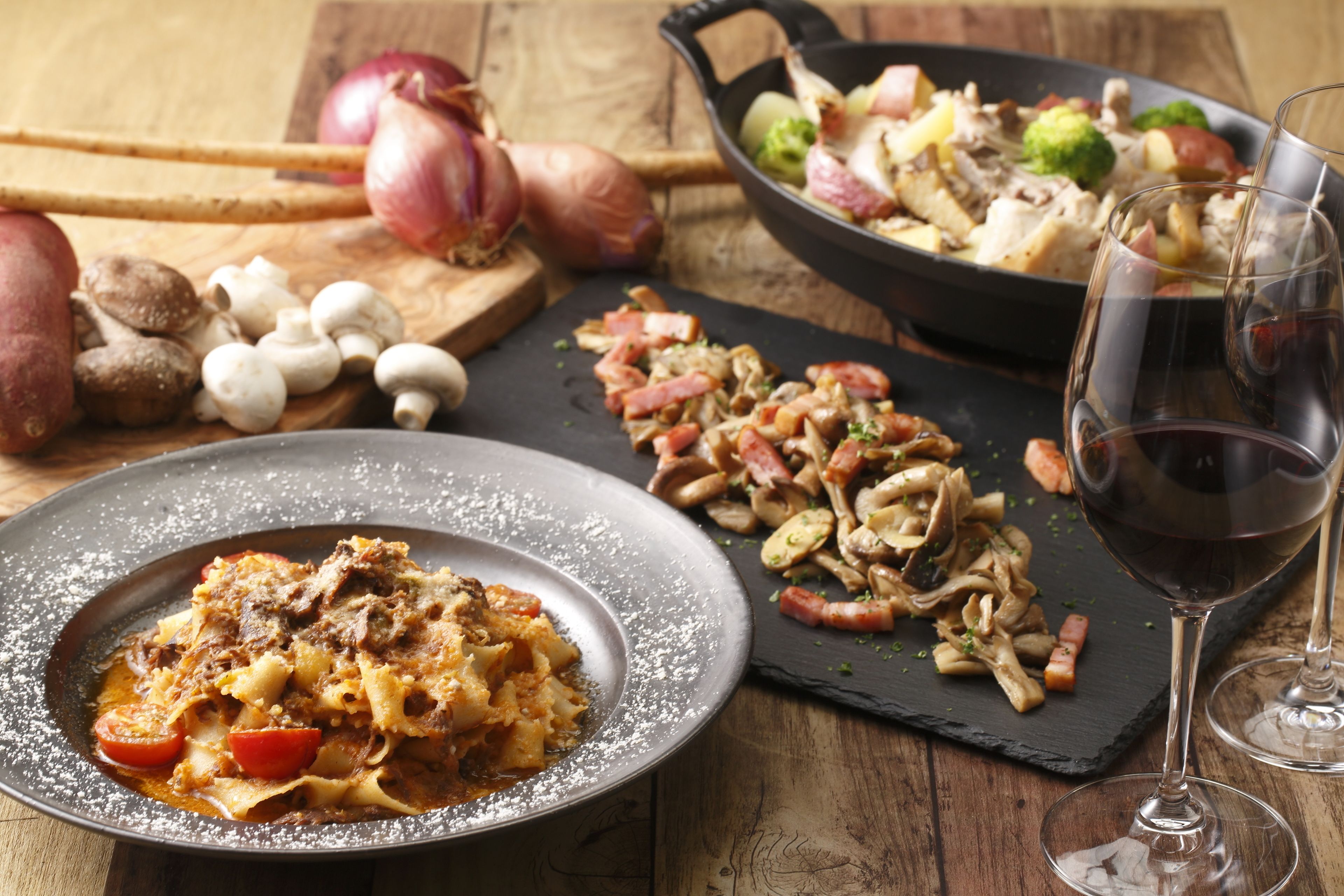 A dining table with a variety of dishes, including pasta, vegetables, and meat, along with two glasses of red wine.