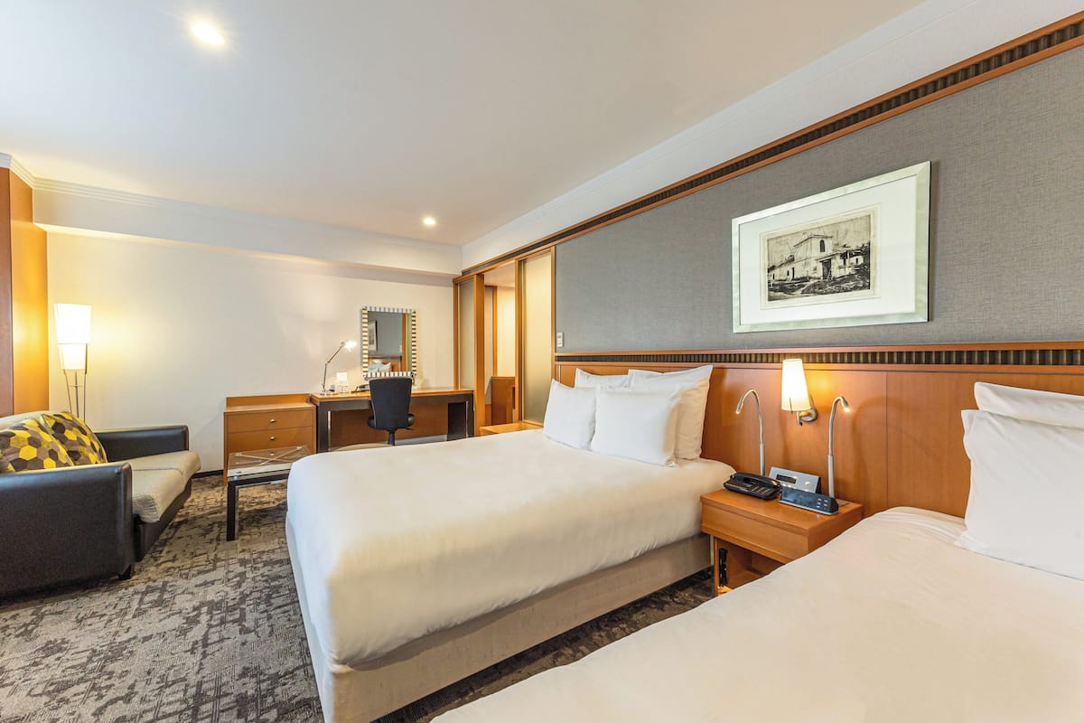 Une chambre d’hôtel avec deux lits, un bureau, une chaise, une lampe et un tableau encadré au mur.