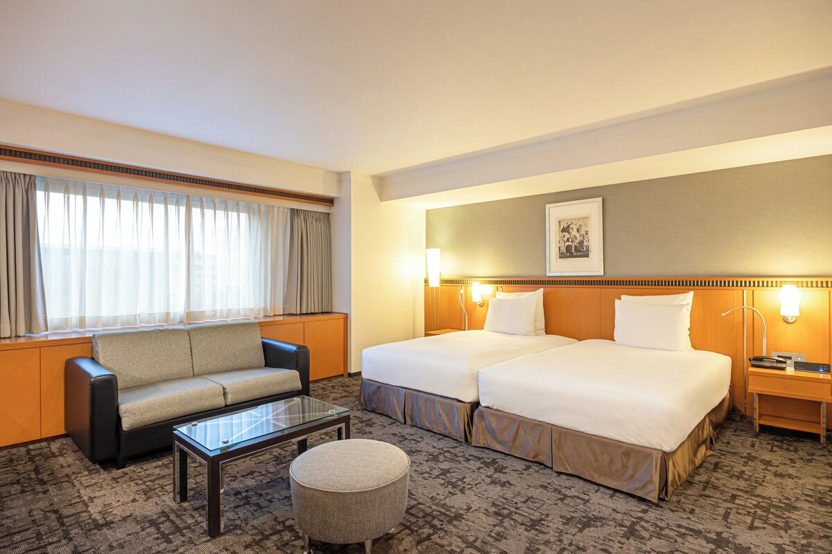 A hotel room with two beds, a sofa, a coffee table, and a lamp.