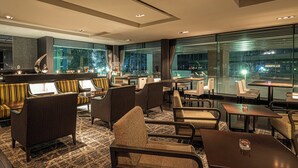 A modern hotel lobby with seating areas, a bar, and large windows offering city views.