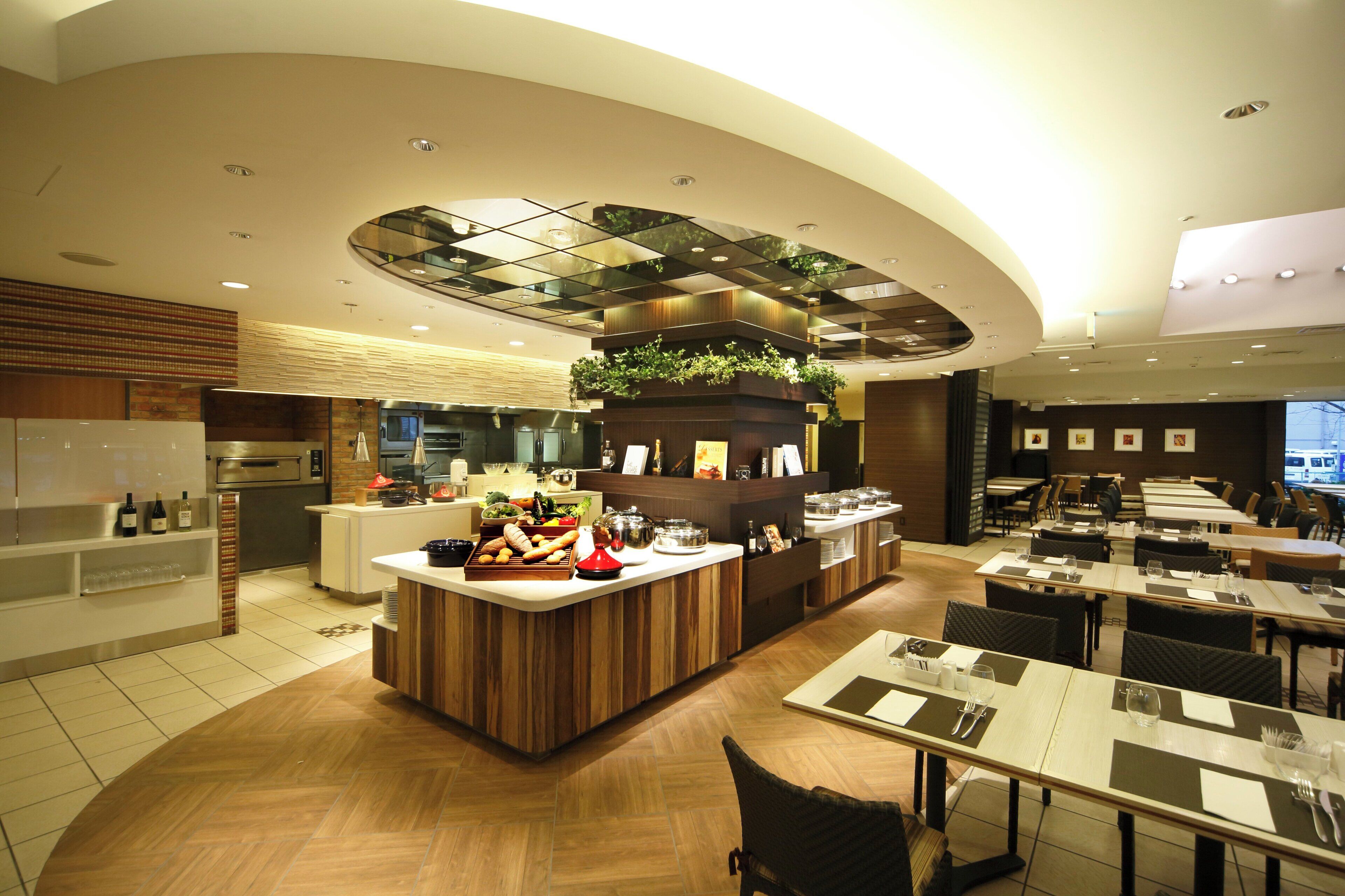 A modern restaurant with a central counter, dining tables, and a kitchen area.