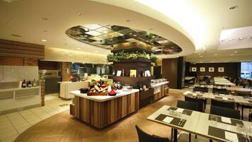 A modern restaurant with a central counter, dining tables, and a kitchen area.