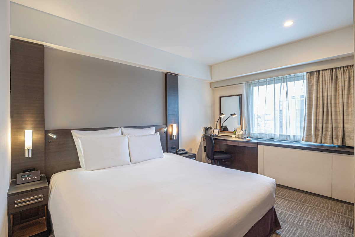 Une chambre d’hôtel avec un grand lit, des tables de chevet, un bureau et une fenêtre avec des rideaux.