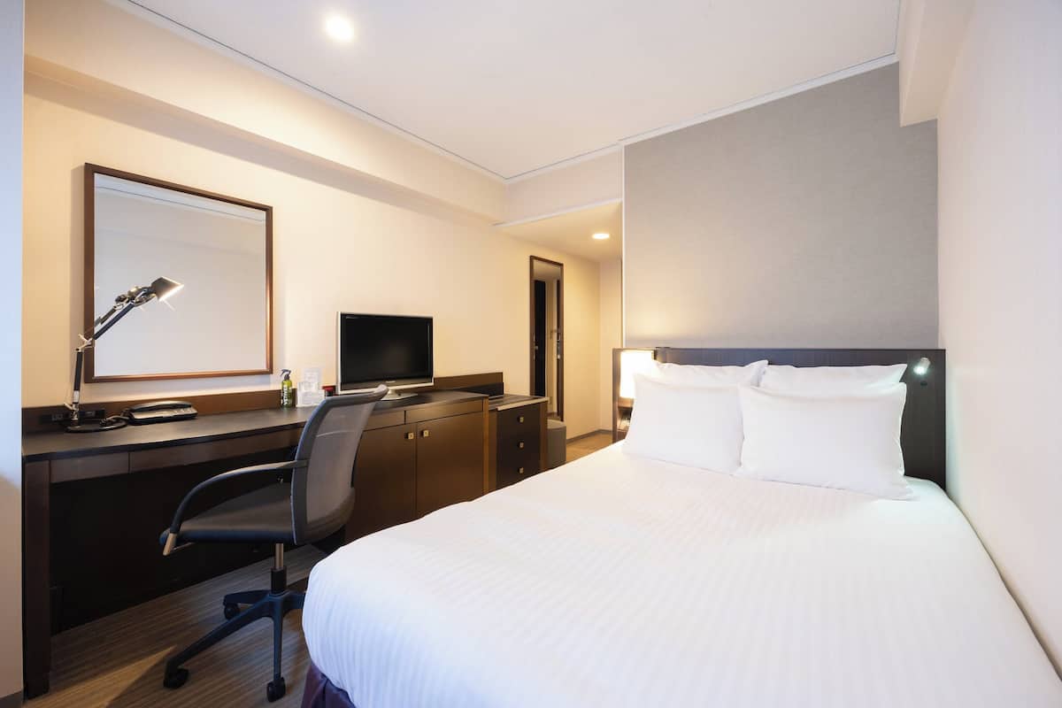 Une chambre d’hôtel équipée d’un lit, d’un bureau, d’une chaise, d’une télévision et d’un miroir.