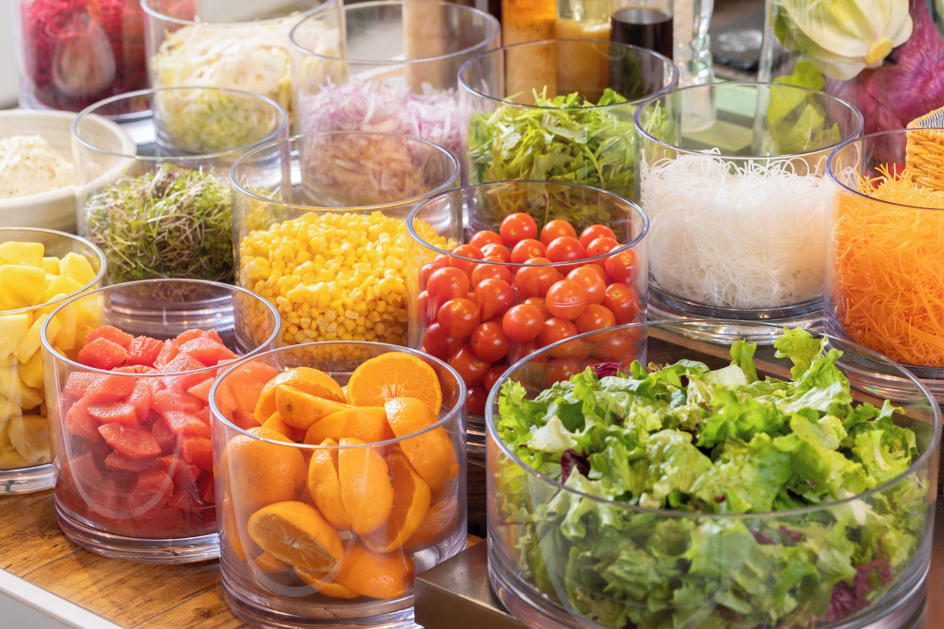 On trouve une variété d’aliments dans des récipients transparents, notamment des fruits, des légumes et du fromage râpé.
