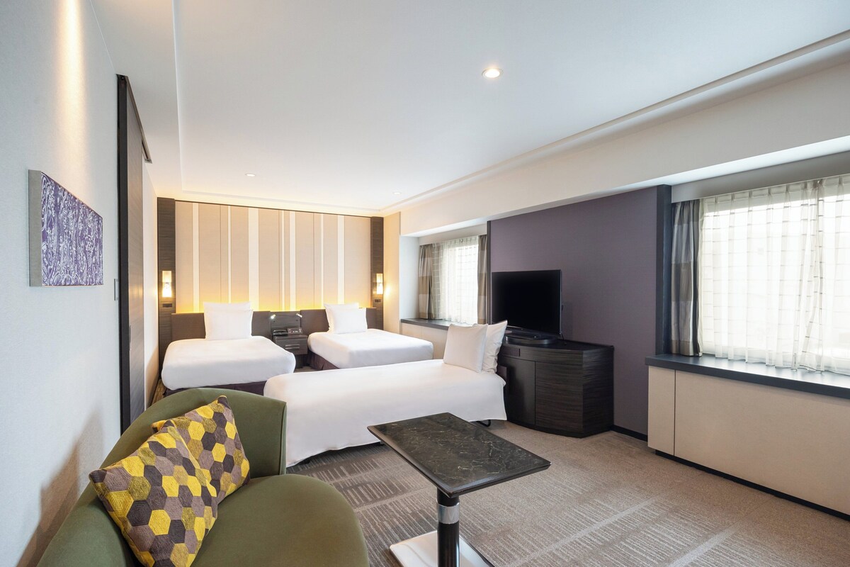 A hotel room with two single beds, a sofa, a TV, and a small table.