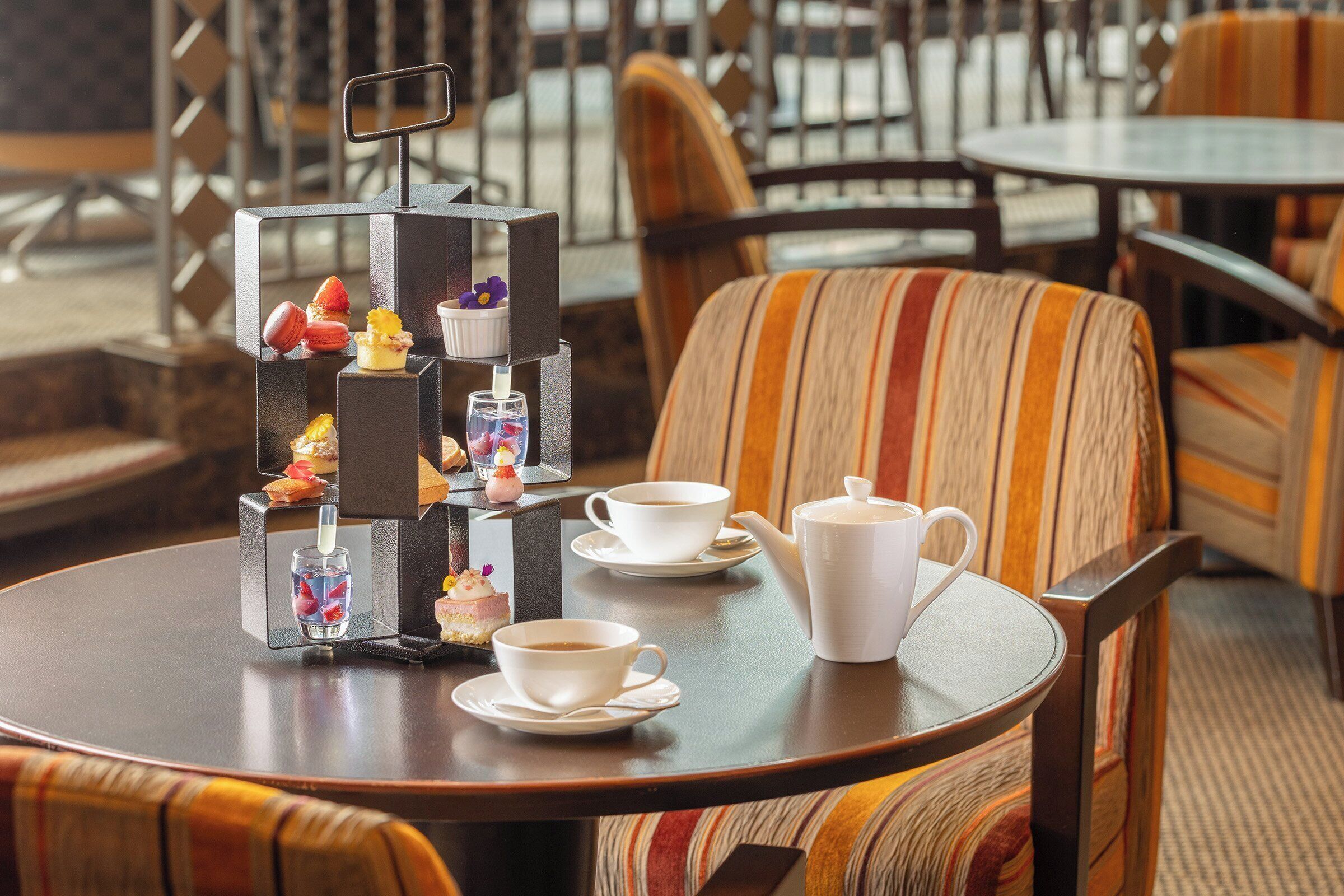 A round table with a teapot, two cups, and a tiered display of macarons and small desserts.