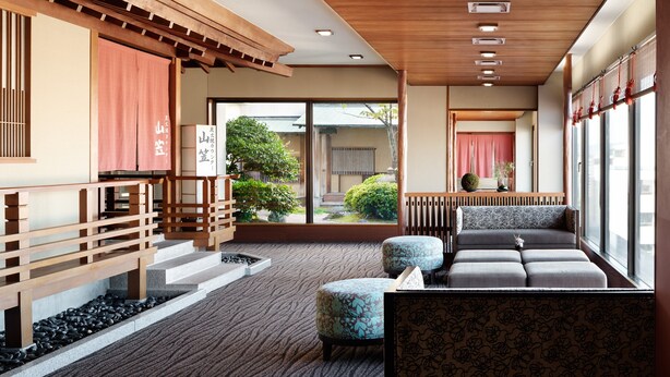 Interior tradicional em estilo japonês, com piso de tatame, um banco de madeira baixo e vista para um jardim através de grandes portas corrediças.
