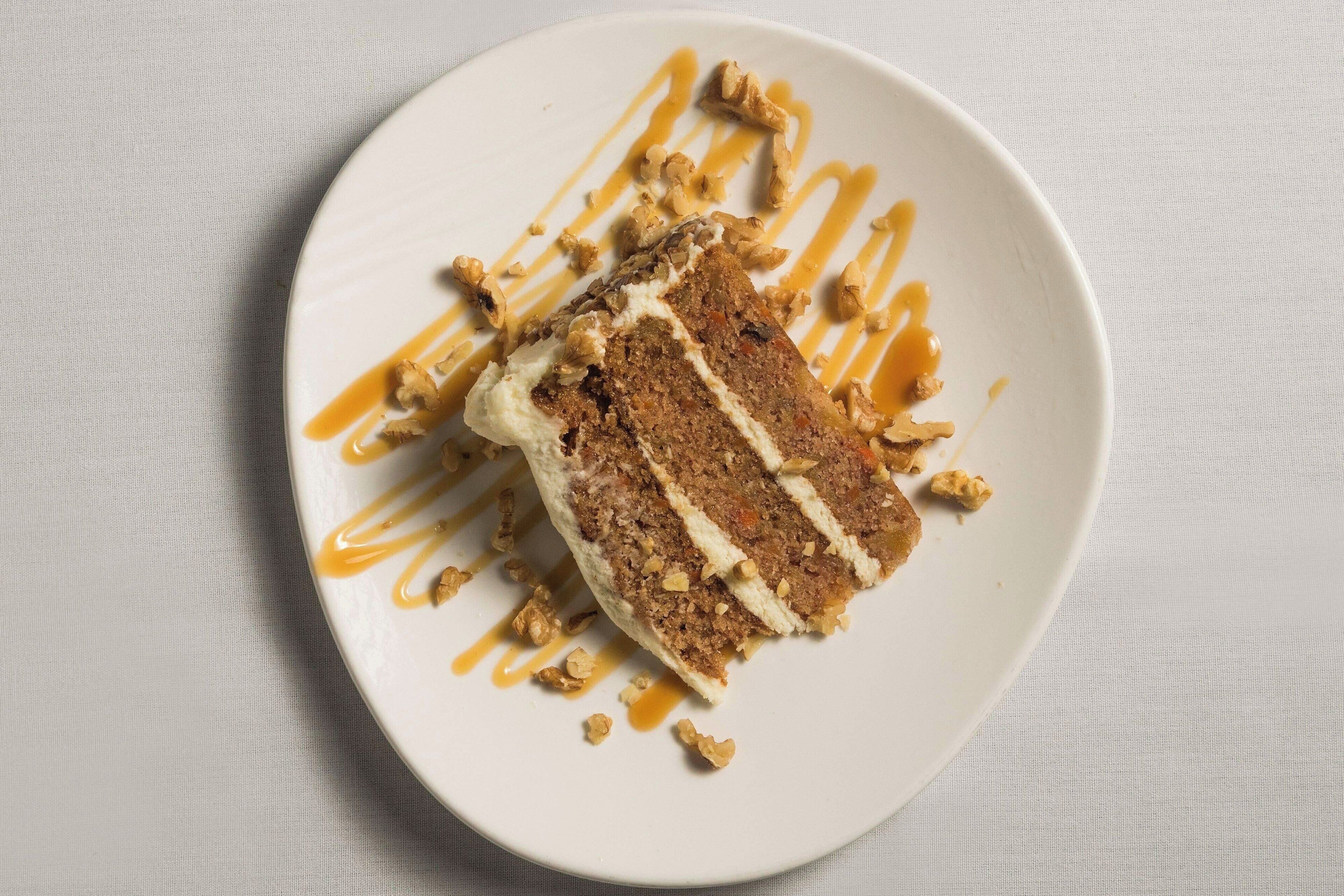 Uma fatia de bolo de cenoura com cobertura de creme e calda de caramelo em um prato.