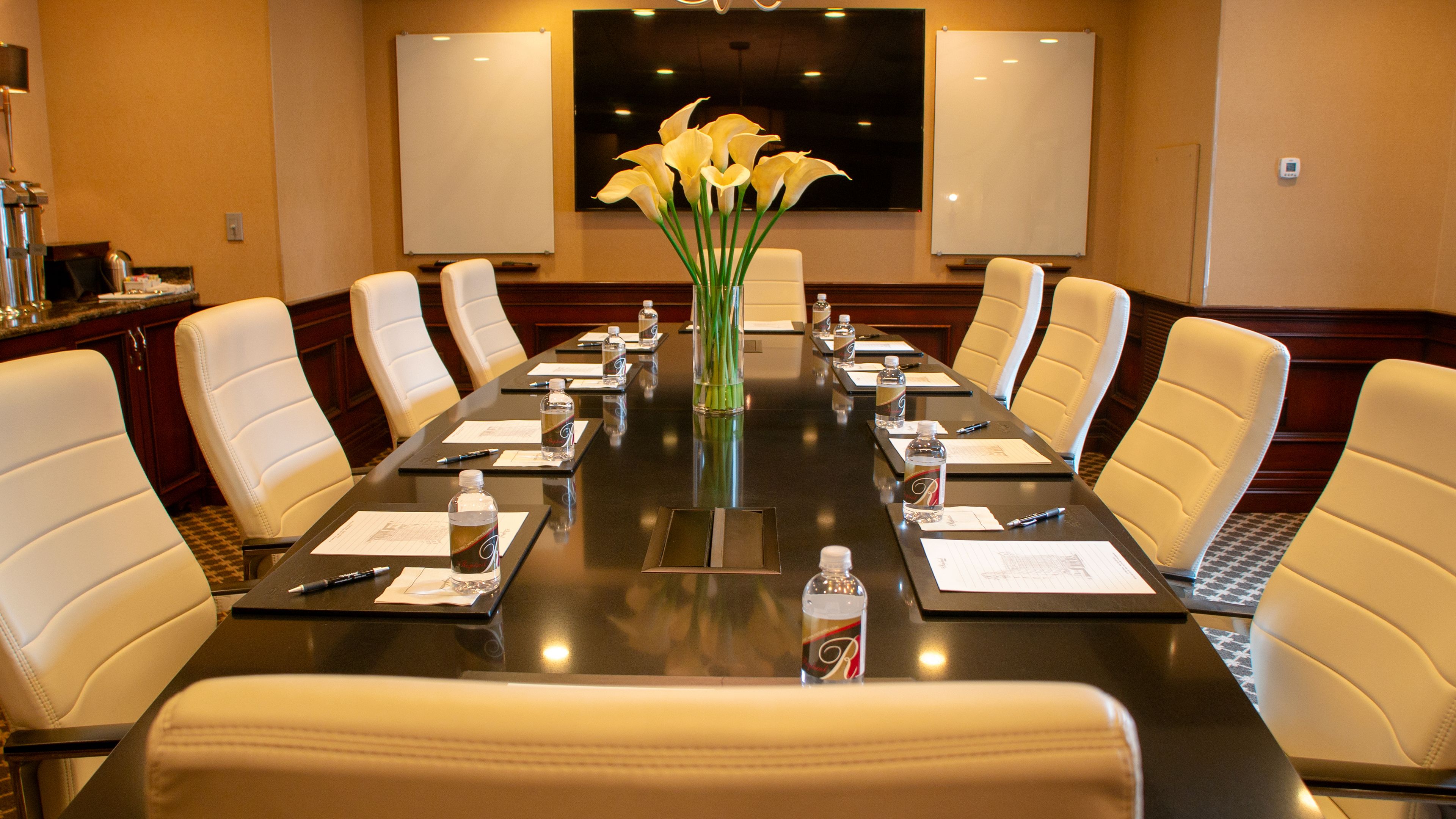 A conference room with a long table, white chairs, and a vase of flowers.