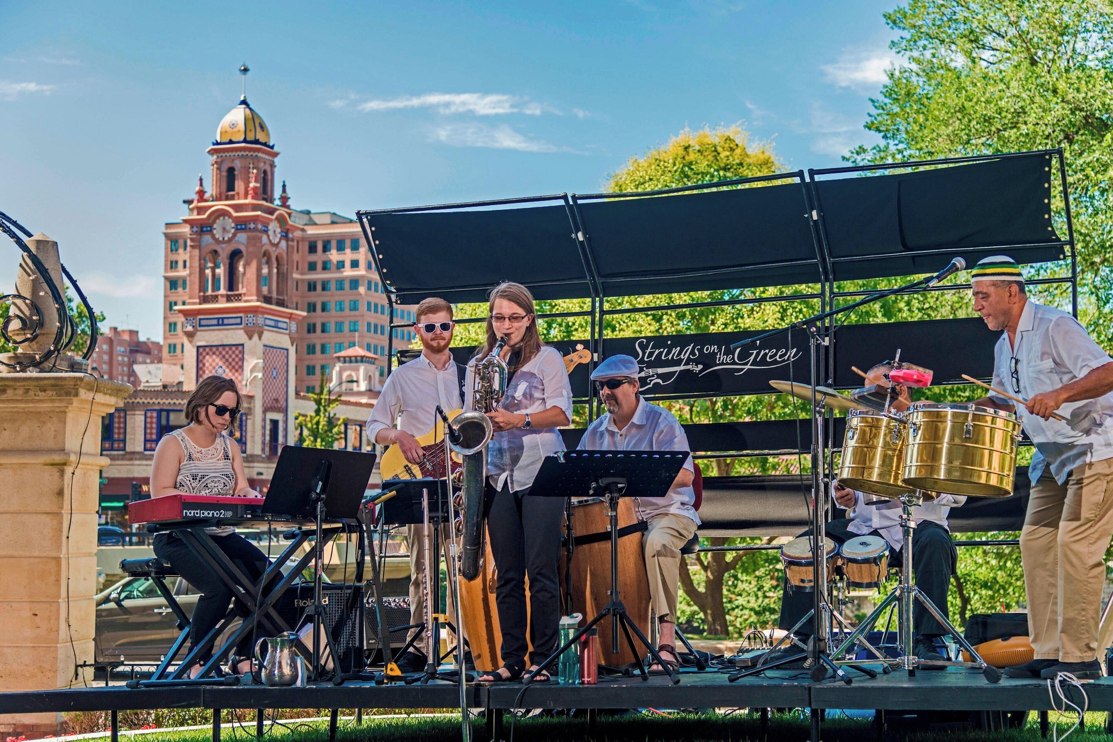 A band performing on an outdoor stage with a cityscape in the background.