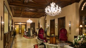 A grand lobby with a chandelier, red upholstered chairs, and a reception desk. - The Raphael Hotel, Autograph Collection (Kansas City)