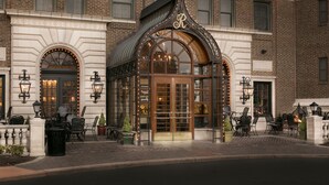A hotel entrance with a glass door, a brick facade, and outdoor seating. - The Raphael Hotel, Autograph Collection (Kansas City)