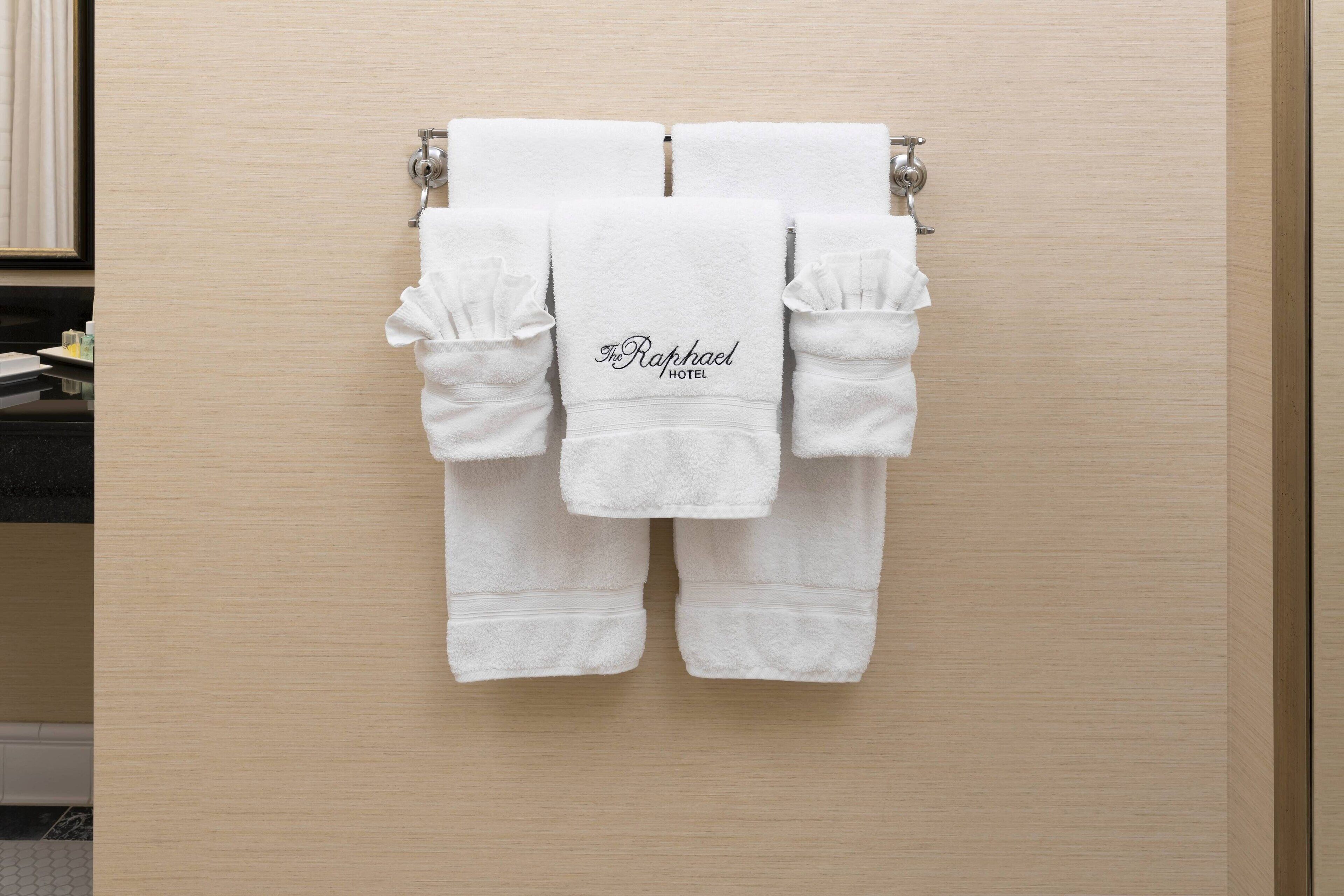 A set of white towels with the text "The Raphael Hotel" hanging on a wooden wall.