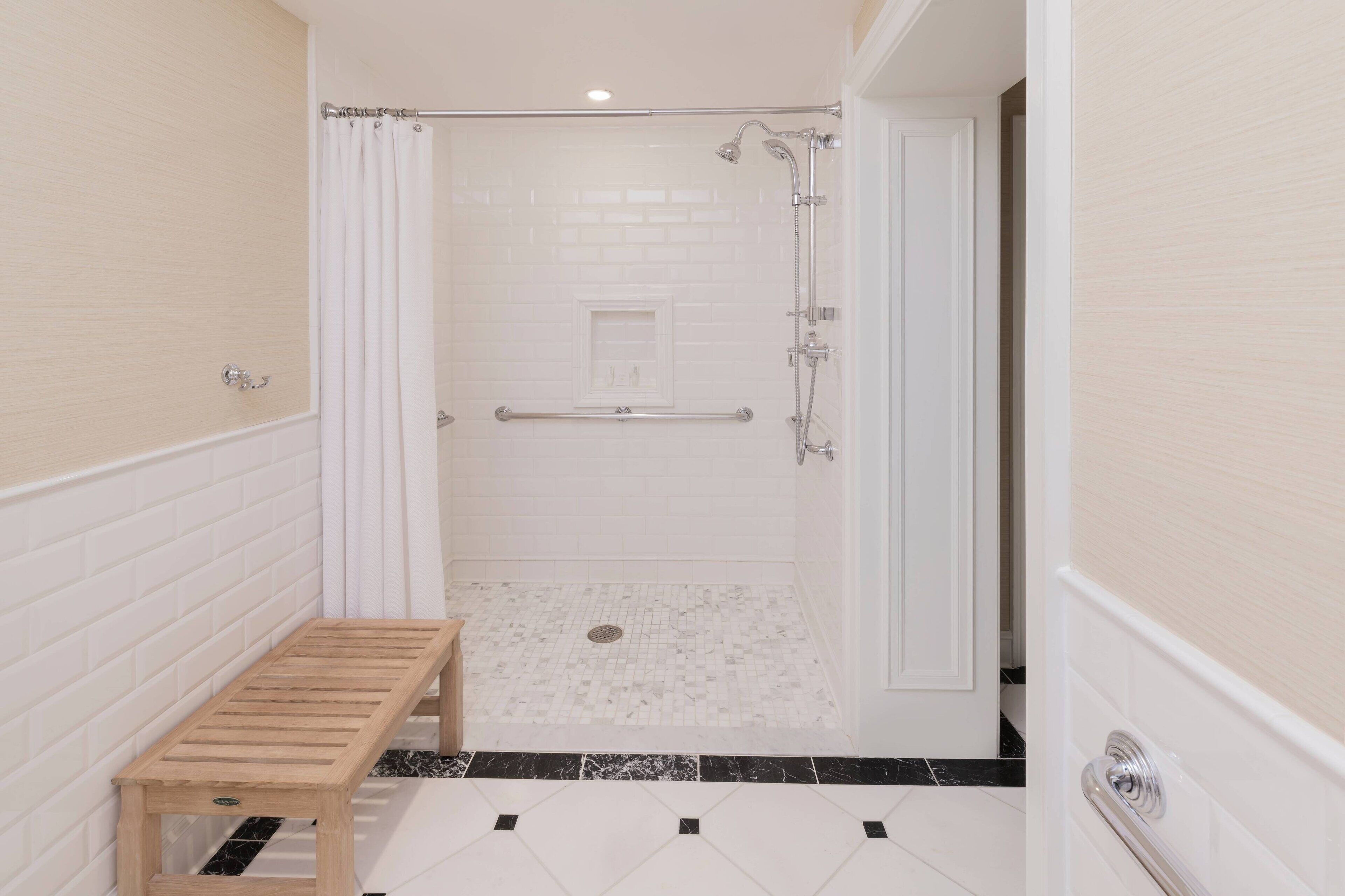 Un petit espace de douche fermé, doté d’un banc, de murs recouverts de carreaux blancs et d’un sol carrelé en noir et blanc.