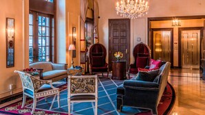 A spacious lobby with a chandelier, two elevators, and a blue patterned carpet. - The Raphael Hotel, Autograph Collection (Kansas City)