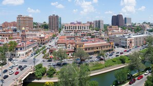 A cityscape with a mix of historic and modern buildings, a river running through the center, and a busy street with cars.