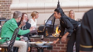 A group of people dining outdoors with a brick wall and a fire feature in the background.